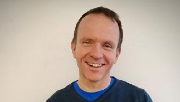 Holmboeprisvinner 2022, Tor Espen Kristensen. Mann med blå genser som smiler på hvit bakgrunn. . 16:9-format. 